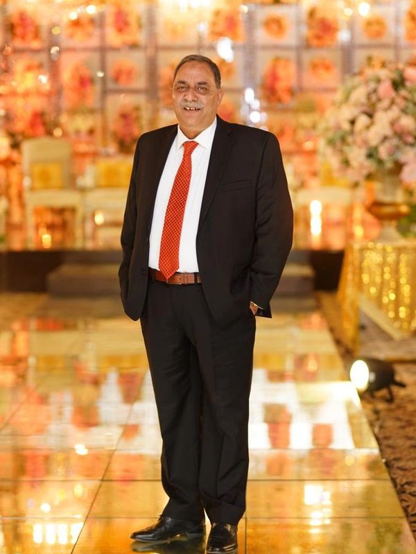 Man in black suit and red tie standing on a reflective floor with floral decorations.
