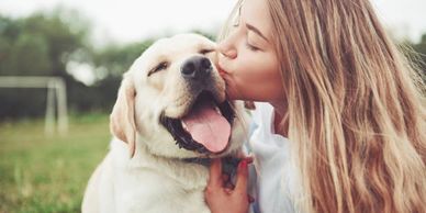 A woman lovingly kisses her happy Labrador dog outdoors.