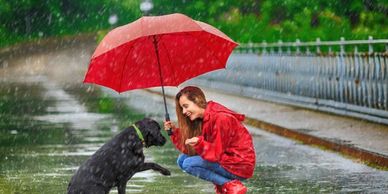 Woman in red jacket holding umbrella for dog in the rain.