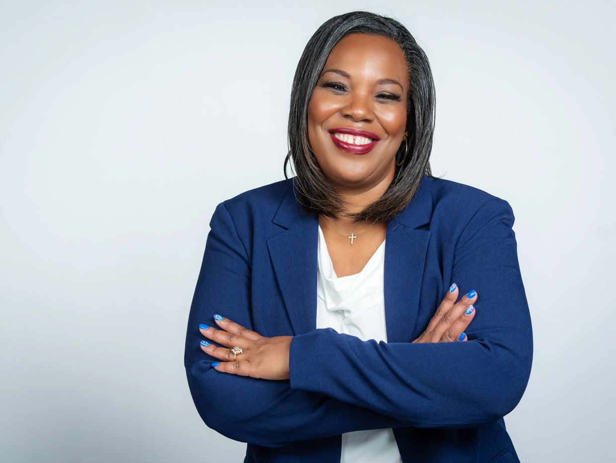 Confident woman smiling with arms crossed, wearing a blue blazer.