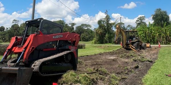 Two excavators working on a grassy area under a blue sky.