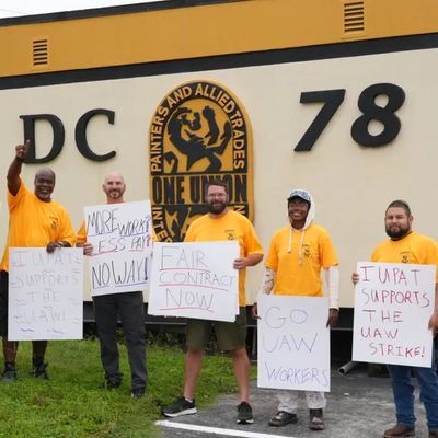A group of people in orange shirts holding protest signs outside a building.