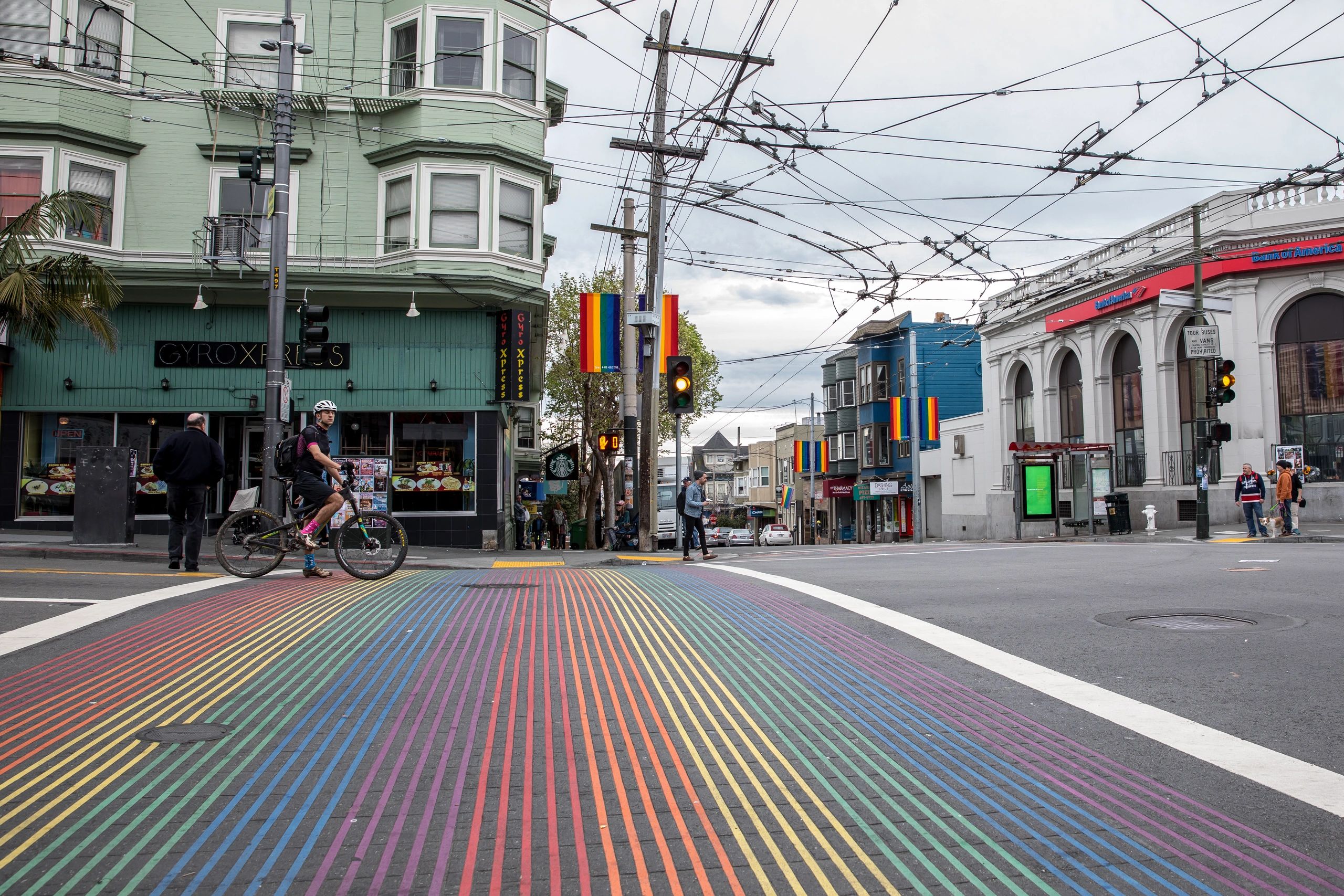 A rainbow-striped crosswalk on a city street with people and buildings.