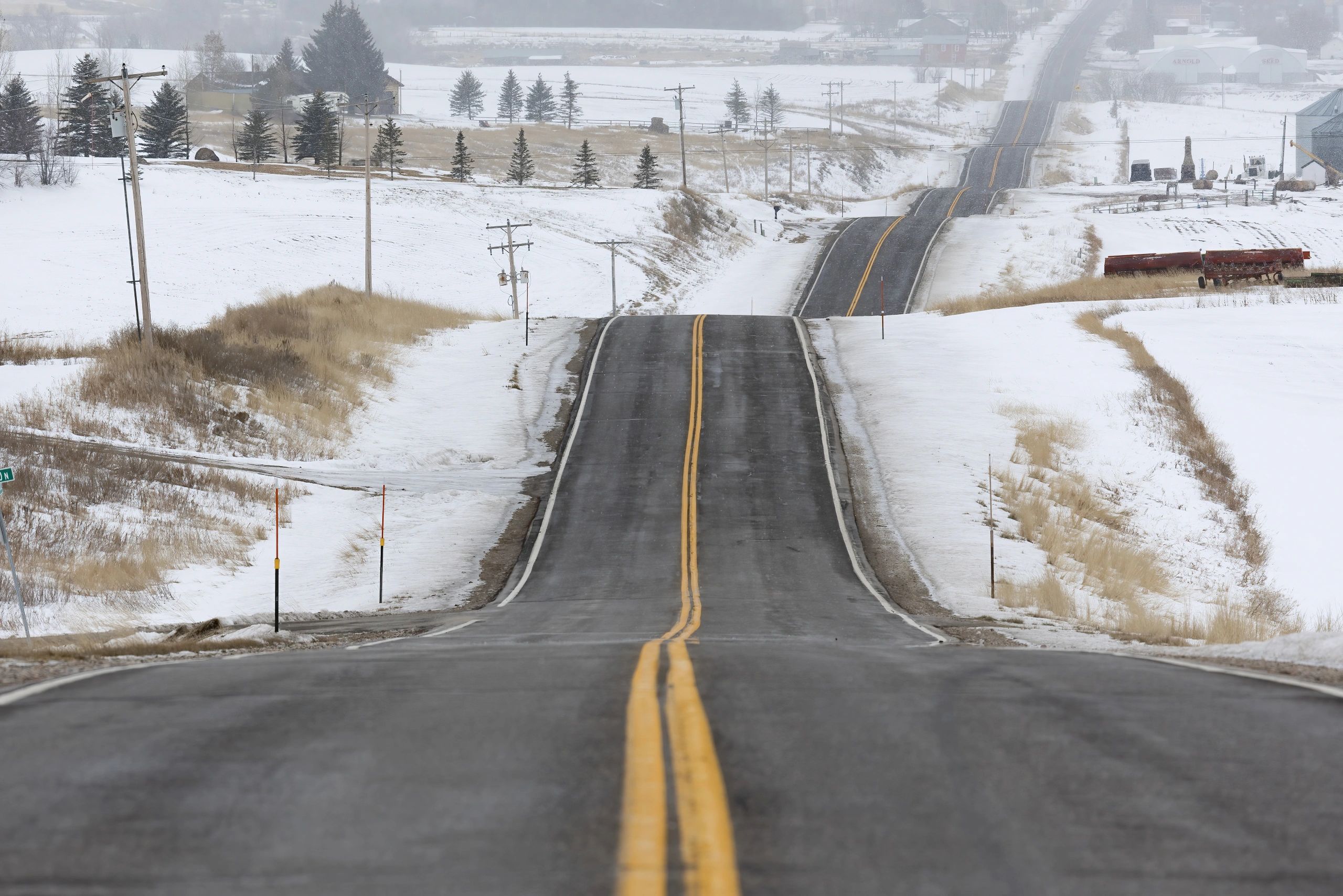A long, empty road stretches through a snowy rural landscape in winter.