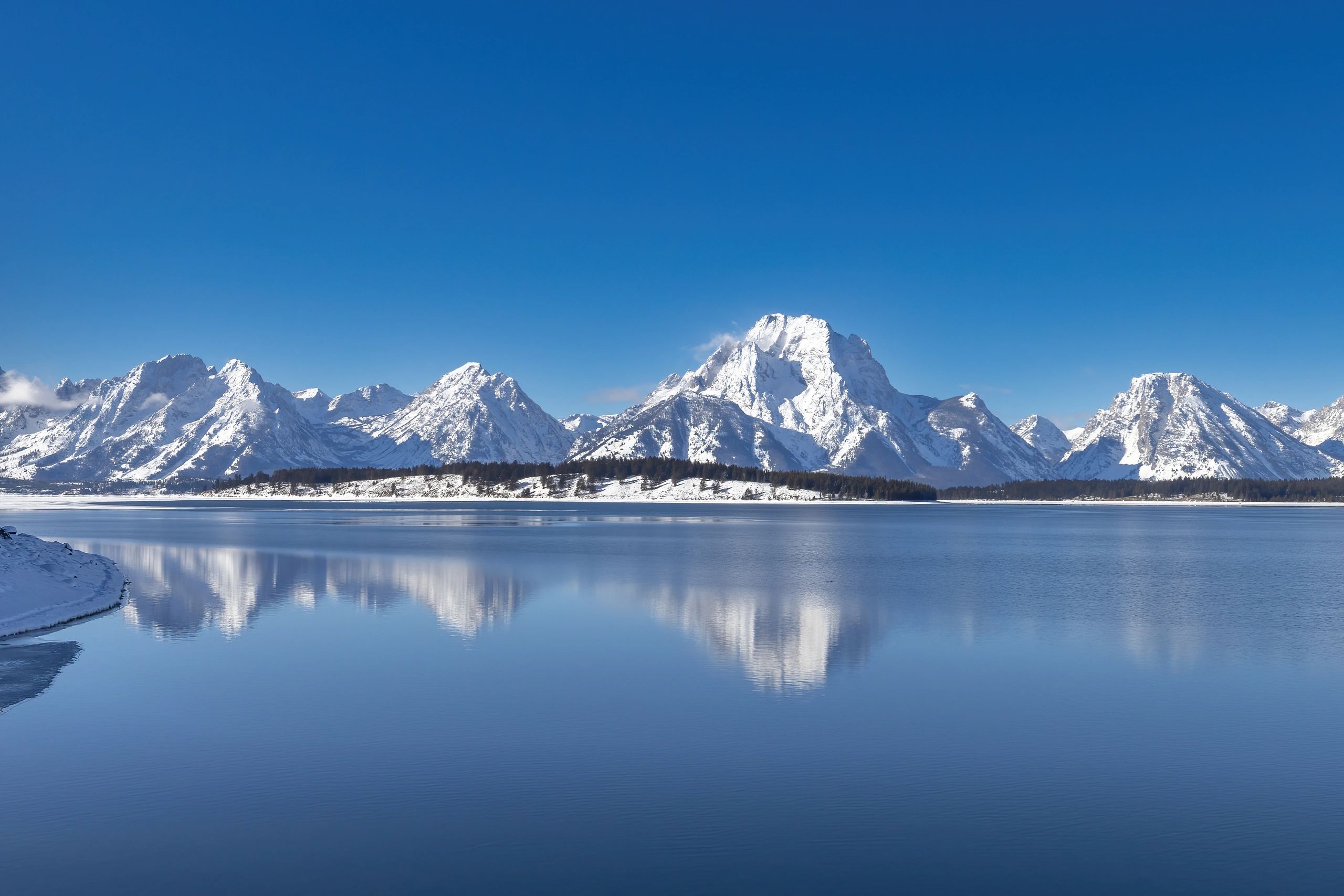 Snow-covered mountains reflected in a calm lake under a clear blue sky.