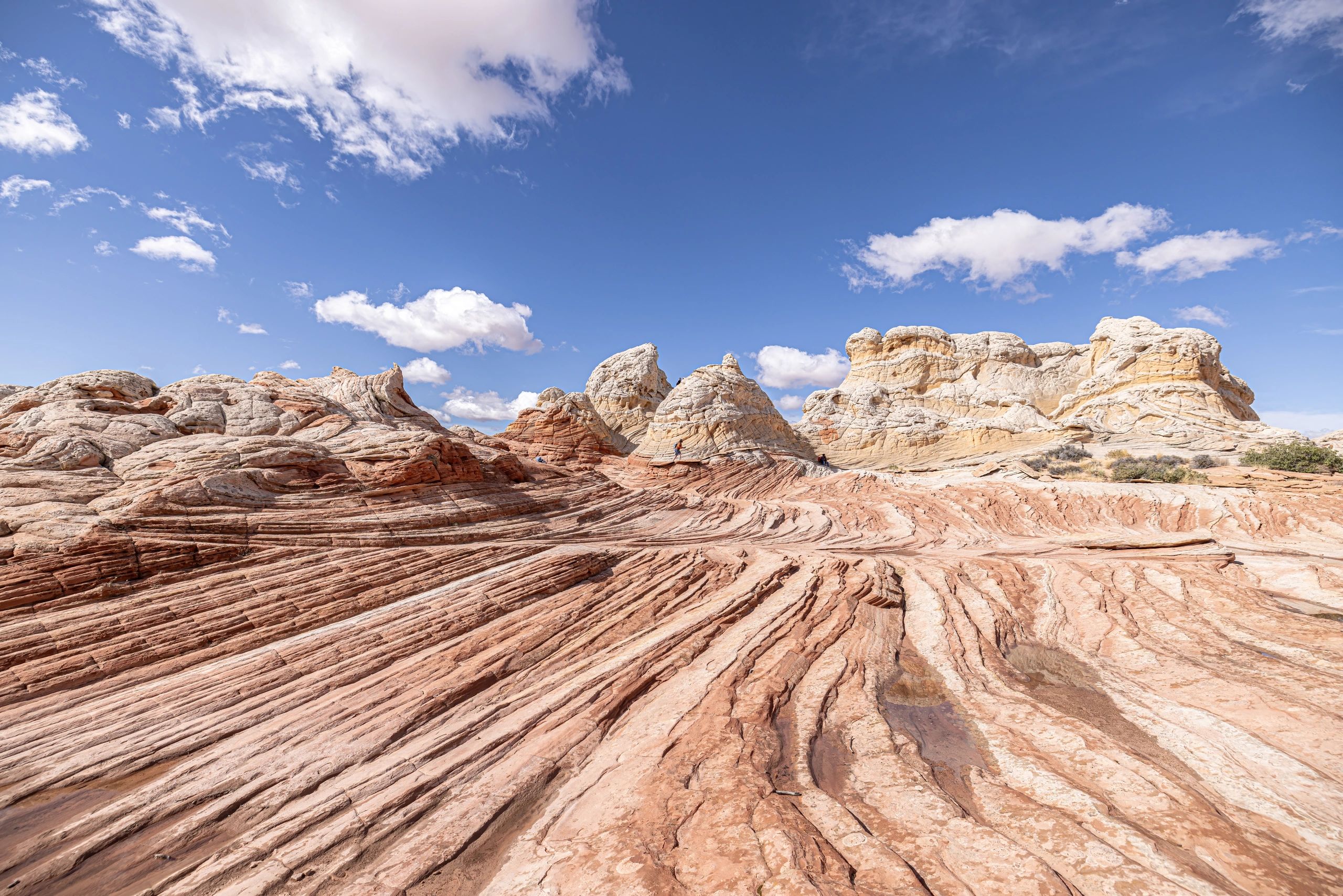 Wavy sandstone formations under a bright blue sky with scattered clouds.