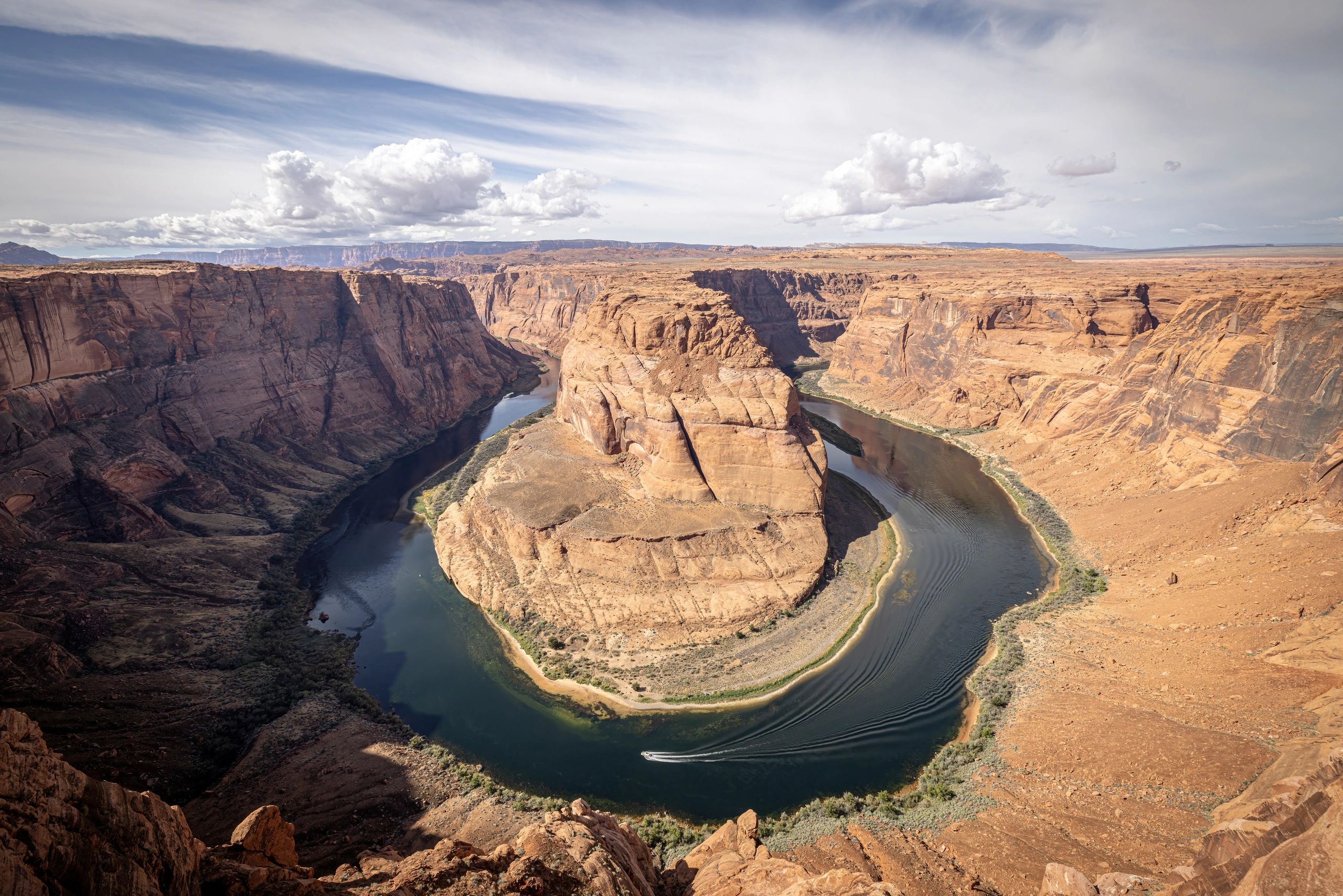 A river bends sharply around a large rock formation in a desert canyon.