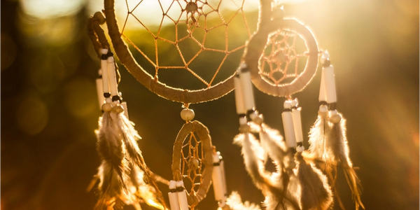 Dreamcatcher glowing warmly in sunlight with feathers and beads.