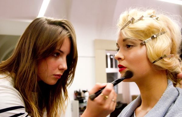 Makeup artist applies foundation on model with blonde hair clips.