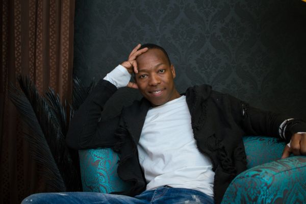 A man in casual clothes relaxing on a teal patterned armchair.
