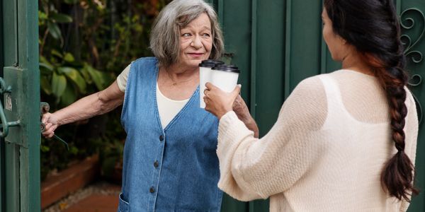 An elderly woman and caretaker drinking coffee together