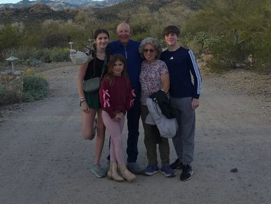 A family of five posing outdoors on a desert trail with mountains in the background.
