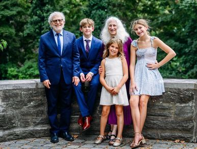 A happy family dressed formally posing outdoors by a stone wall.