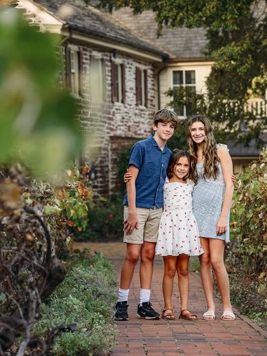 Three siblings posing happily outside a charming house.