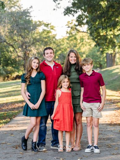 A happy family of five posing outdoors on a sunny day.