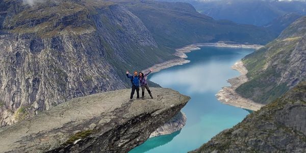 Two people stand on a cliff overlooking a river valley.