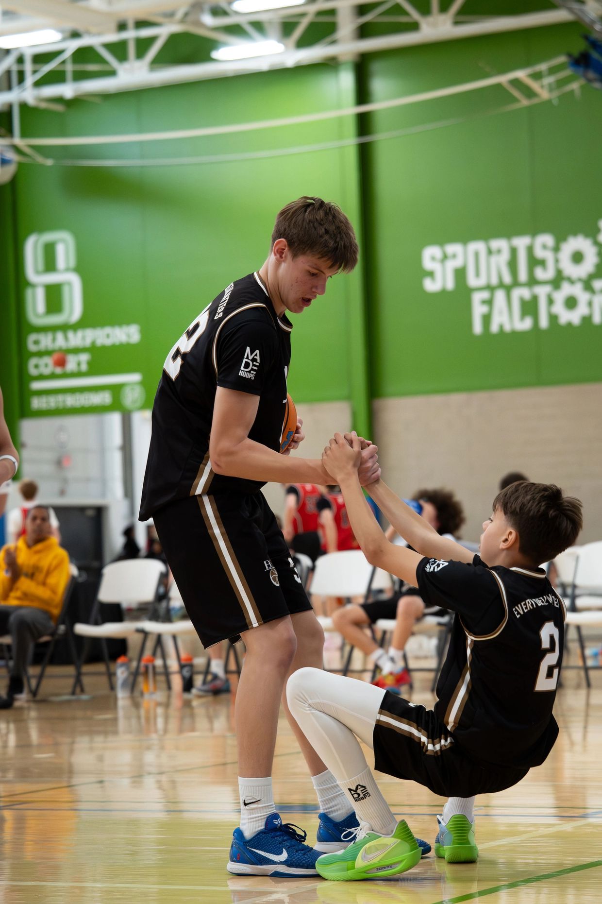 Basketball player helping teammate off the court during a game.