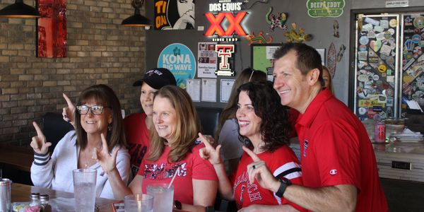 Group of Texas Tech fans smiling and posing with hand signs at a restaurant.