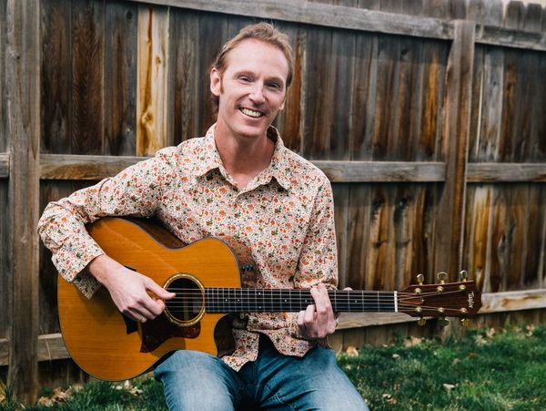 Man smiling while playing acoustic guitar outdoors.