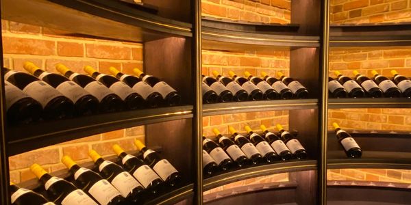 Curved wine cellar shelves neatly stocked with bottles, set against a warm brick wall backdrop