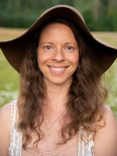 Smiling woman with long curly hair wearing a large brown hat outdoors.