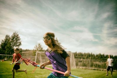 Children playing lacrosse outdoors on a sunny day.