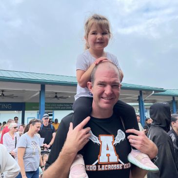 Man carrying a young girl on his shoulders at an outdoor event.