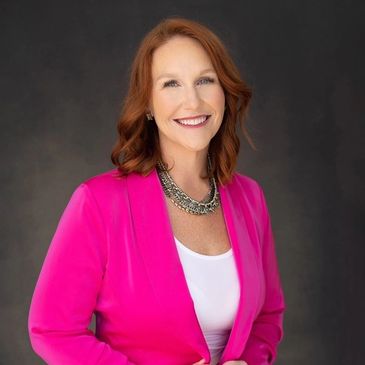 Smiling woman in a bright pink blazer against a dark background.