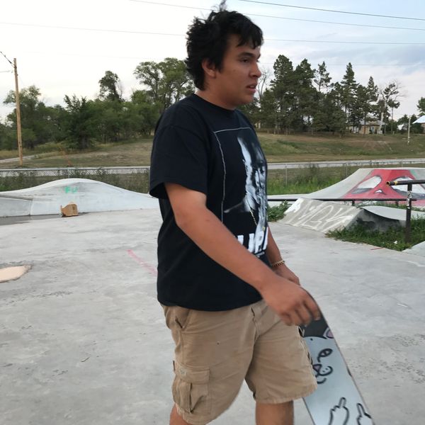 A young man walks with a skateboard at an outdoor skate park.