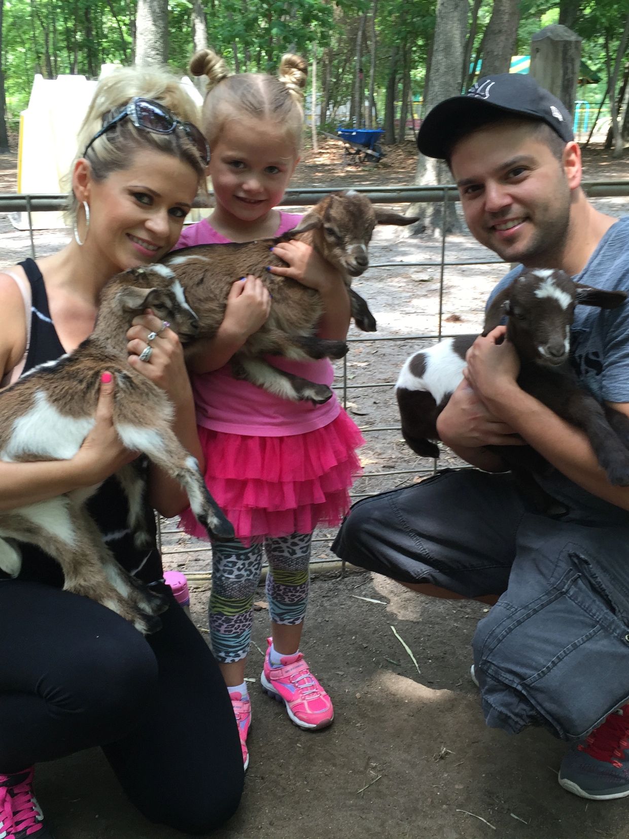 Family smiling and holding baby goats at a petting zoo.