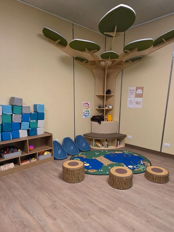 A cozy children's playroom with tree-like shelves and wooden stump stools.