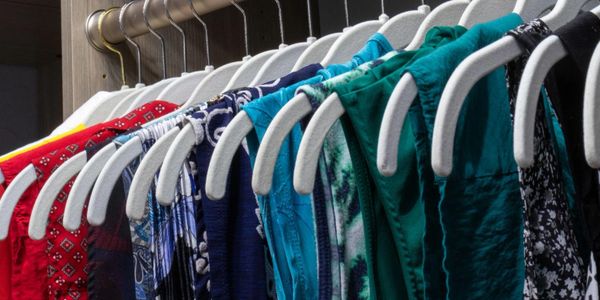 Colorful clothes hanging on white hangers in a closet.