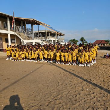 Large group of children in yellow uniforms assembled outdoors on sandy ground.