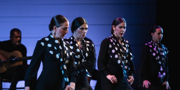 Four women performing flamenco dance in black dresses with polka dot scarves.