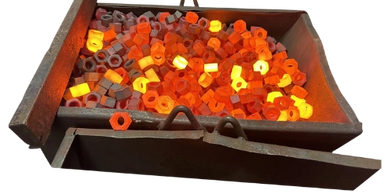 Glowing hot metal hex nuts in a furnace for heating or forging.