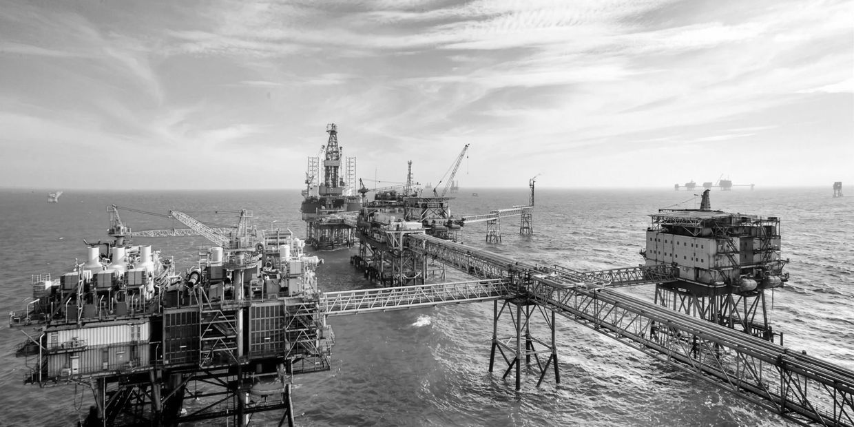 Black and white image of offshore oil rigs connected by bridges over the ocean.