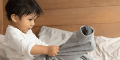 A child folding a gray sweater on a bed.