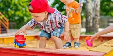 Children playing with toys in a sandbox on a sunny day.