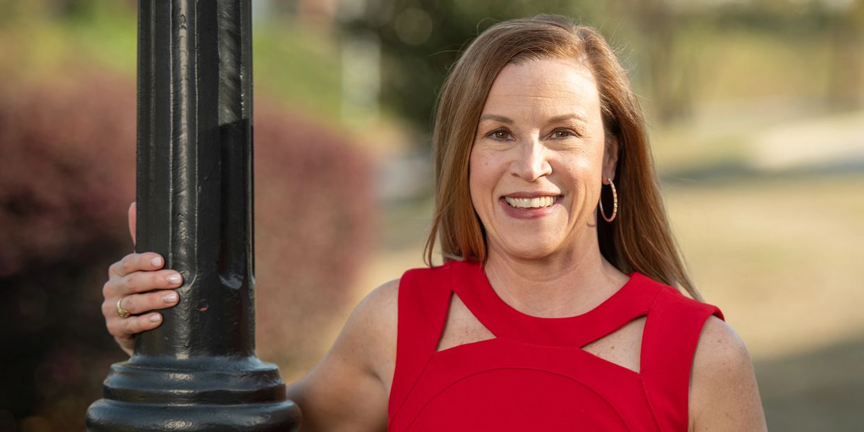 Smiling woman in a red dress holding a black pole outdoors.
