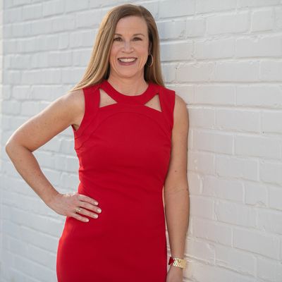 Woman in a red dress smiling by a white brick wall.
