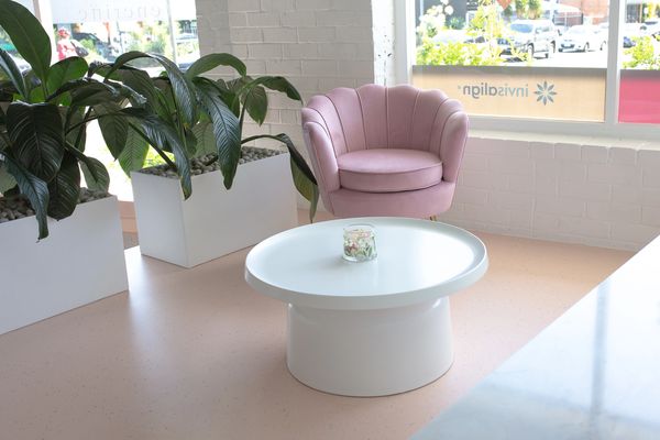 A bright room with lush plants, a peach floor and a comfortable pink armchair.