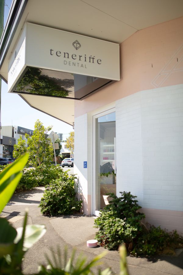 The exterior of Teneriffe Dental with a white sign with black writing and lush green plants.