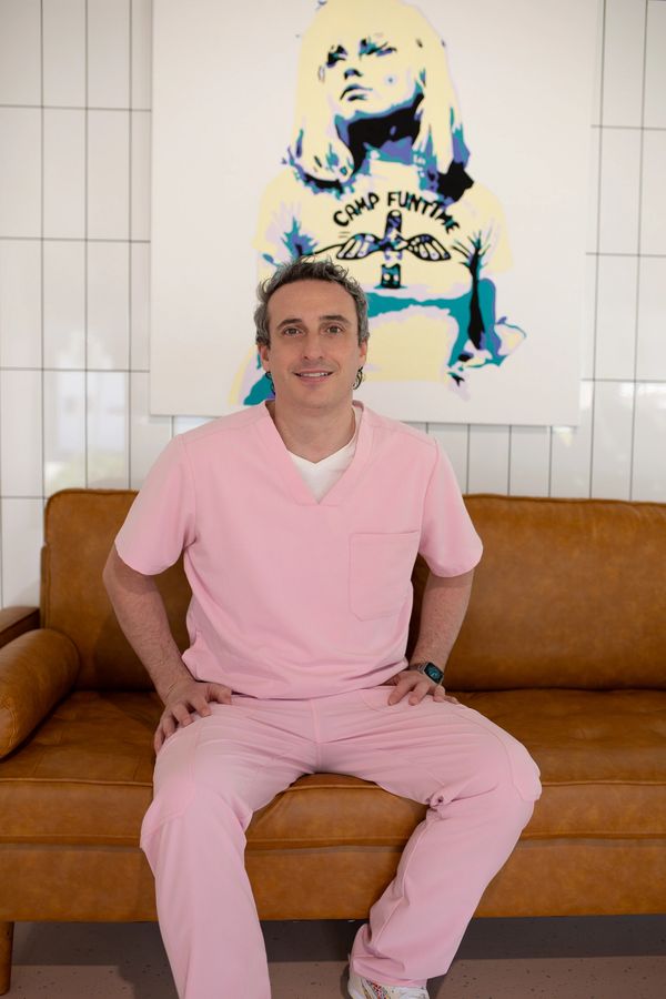Dr Hayden Stewart sitting on a tan leather couch in front of a colourful art piece of Blondie.