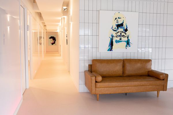 A bright interior with a leather couch in the foreground and a hallway with art in the background.