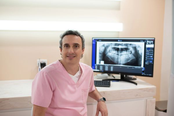 Dr Stewart seated in front of a computer with a dental x-ray displayed. He is wearing pink scrubs.