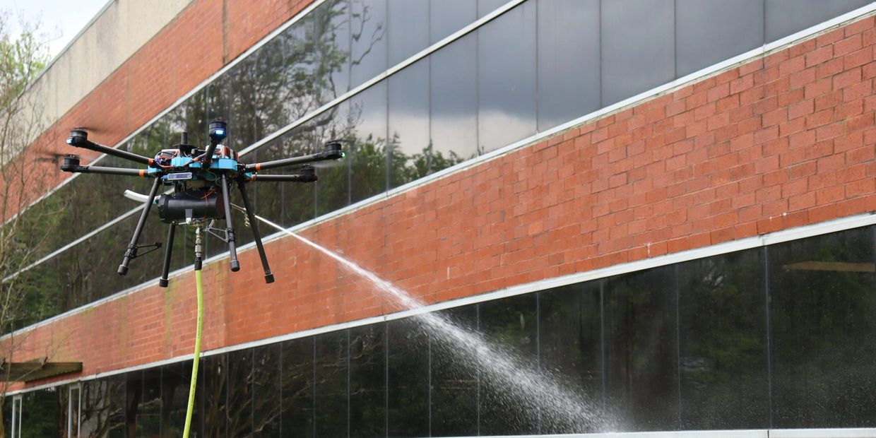 A drone sprays water against a building's glass and brick exterior.