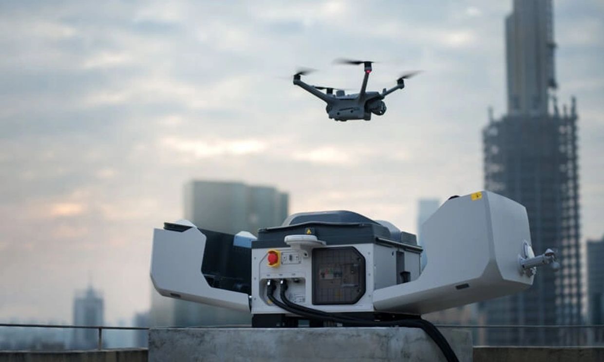 A drone flying near a mechanical device on a rooftop with city buildings in the background.