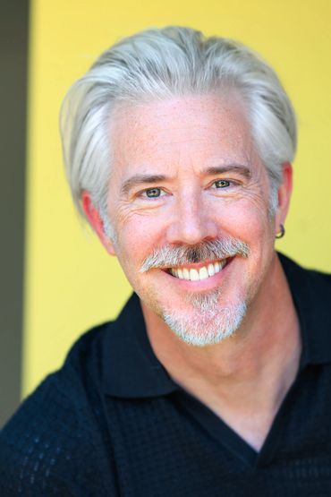 Smiling middle-aged man with gray hair and beard against yellow background.