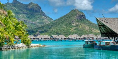Tropical overwater bungalows set against lush green mountains and blue skies.