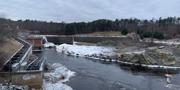 A snowy river with a dam and surrounding forest.